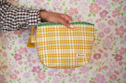 Person holding a yellow checkered pouch with a floral patterned background