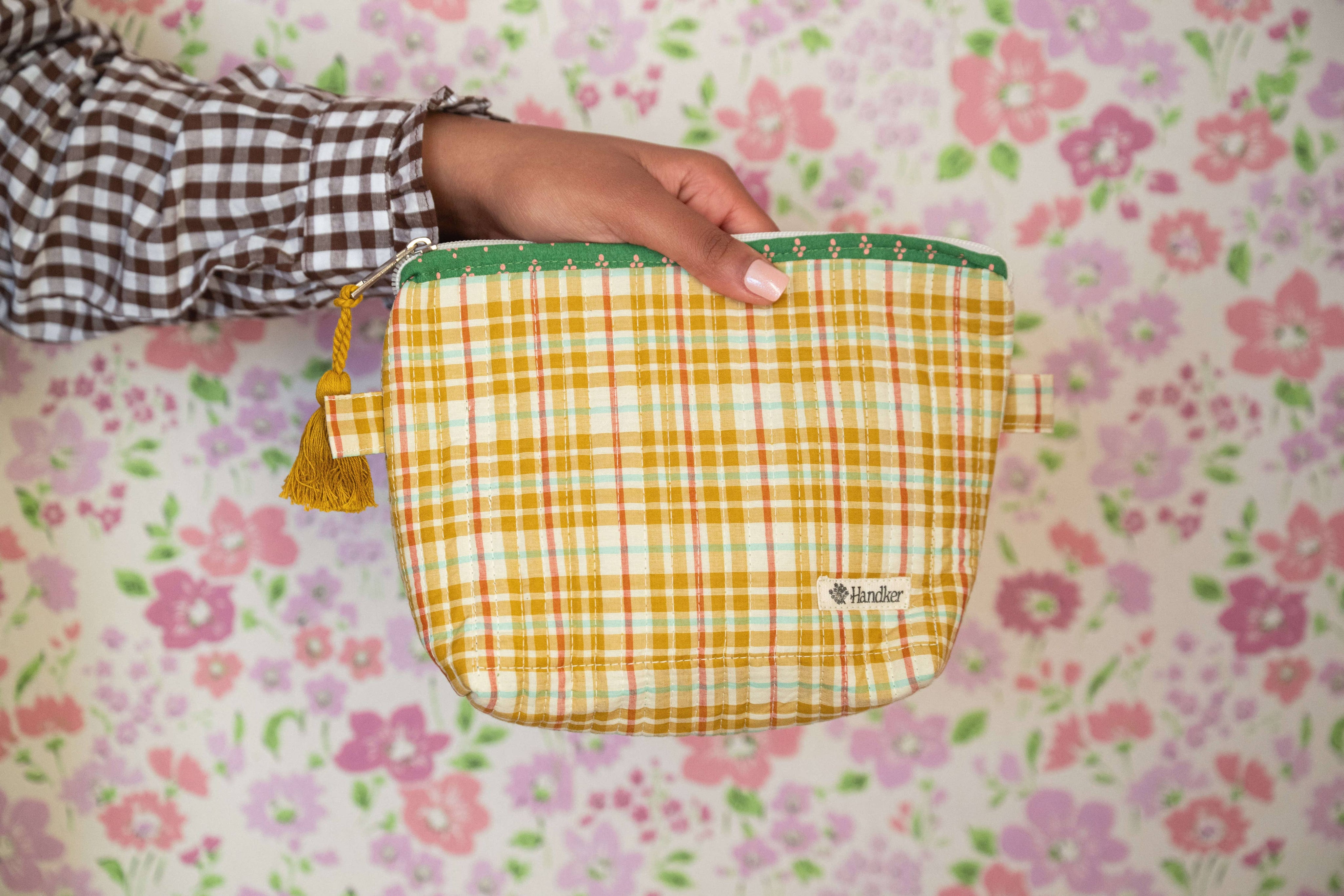 Person holding a yellow checkered pouch with a floral patterned background