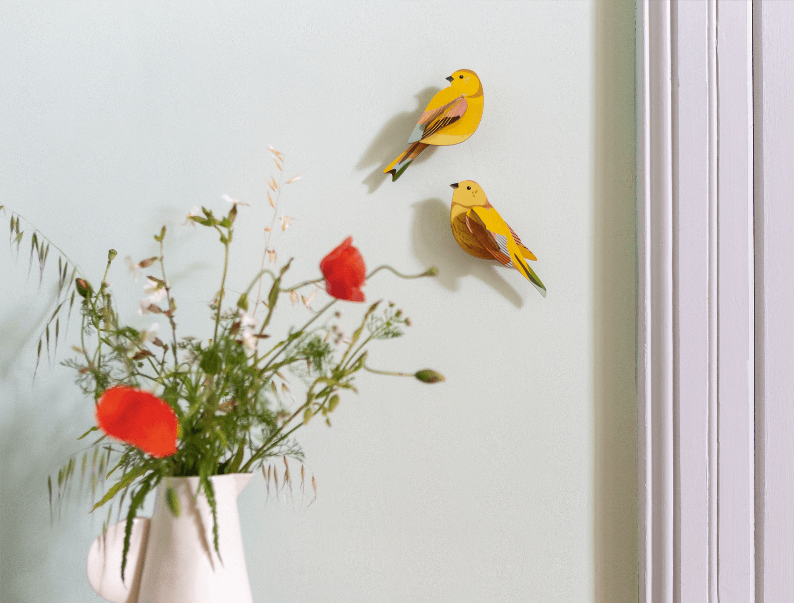 Decorative yellow birds on a white wall with a vase of flowers.