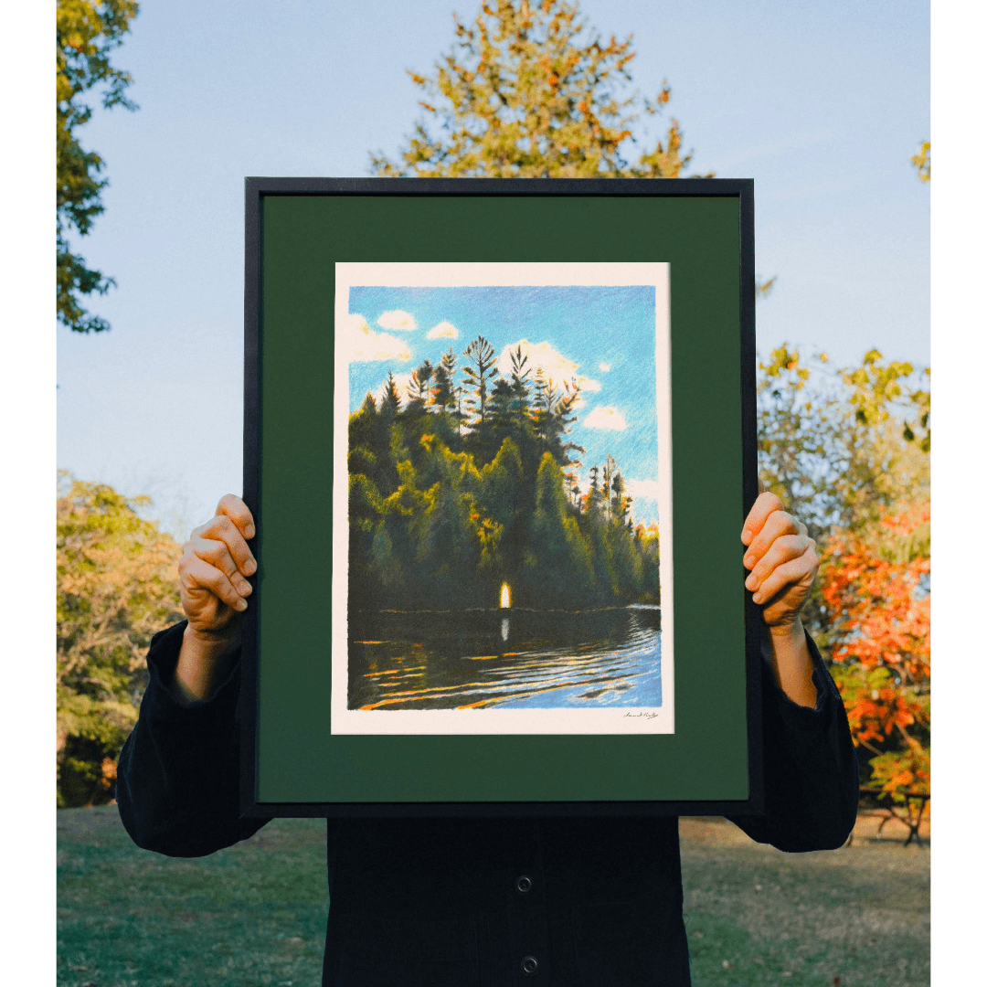 Person holding a framed print of a nature scene with trees and water.