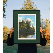 Person holding a framed print of a nature scene with trees and water.