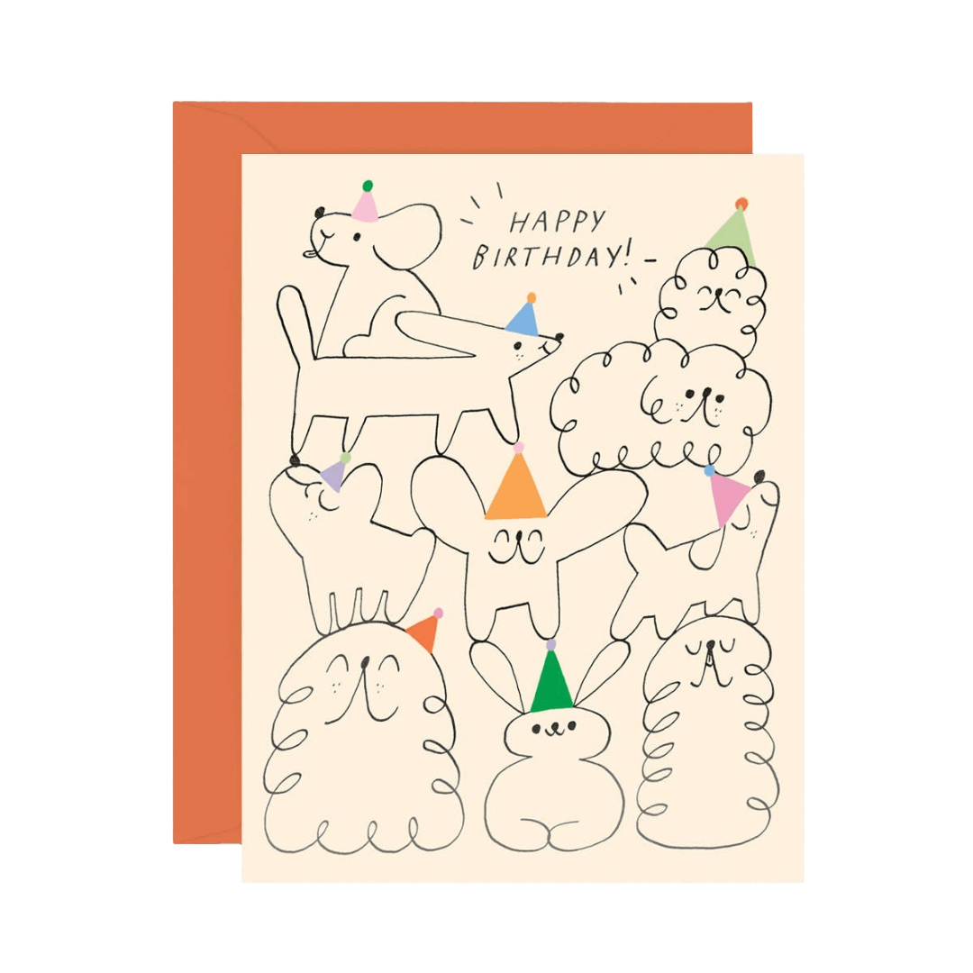 Birthday card with cartoon dogs wearing party hats on a cream background with an orange envelope
