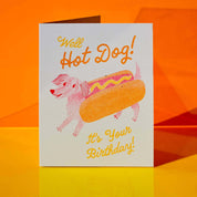 Birthday card with a dog in a hot dog costume on an orange background