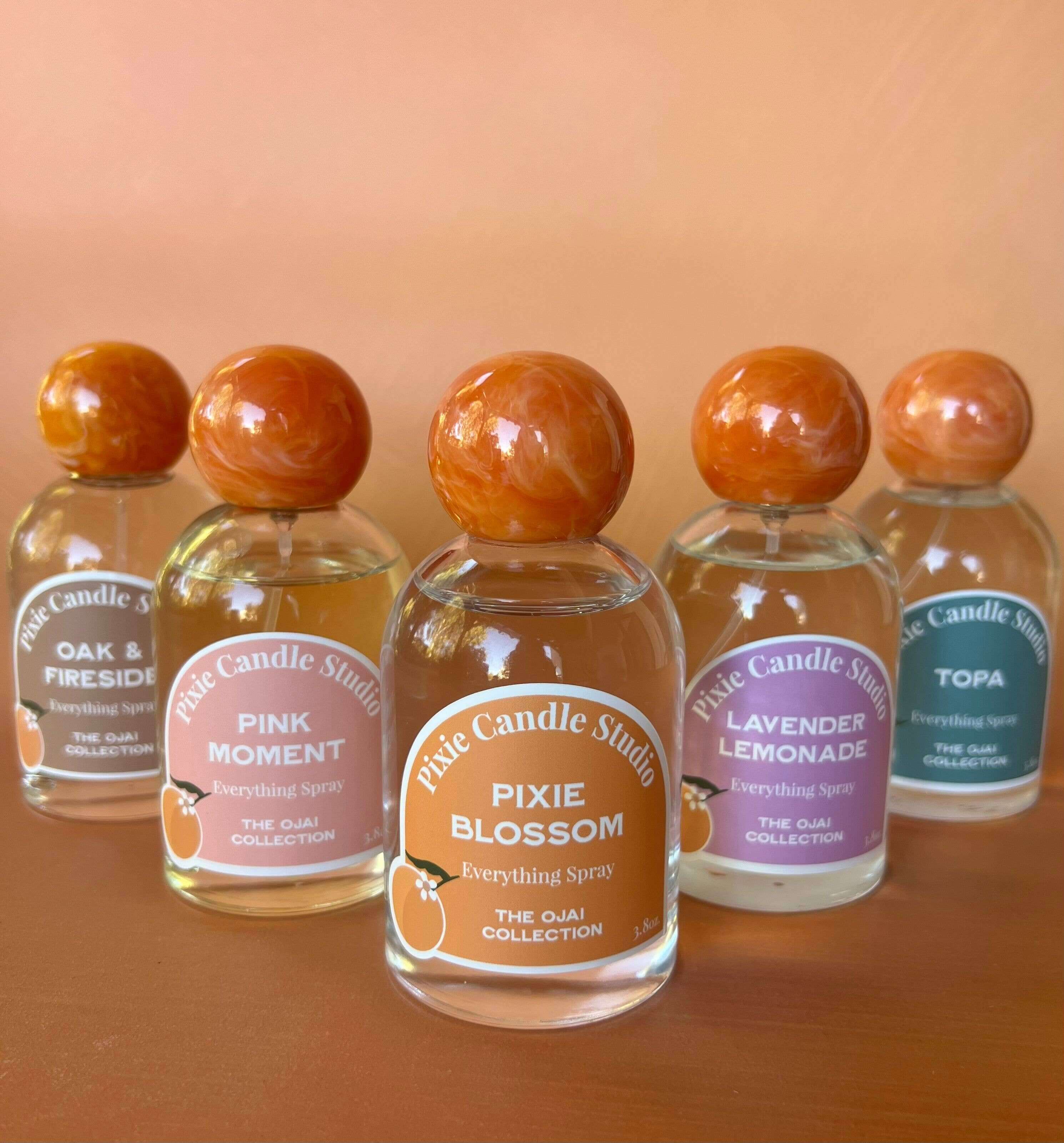 Five bottles of Palo Candle Studio everything spray on a wooden surface with an orange background