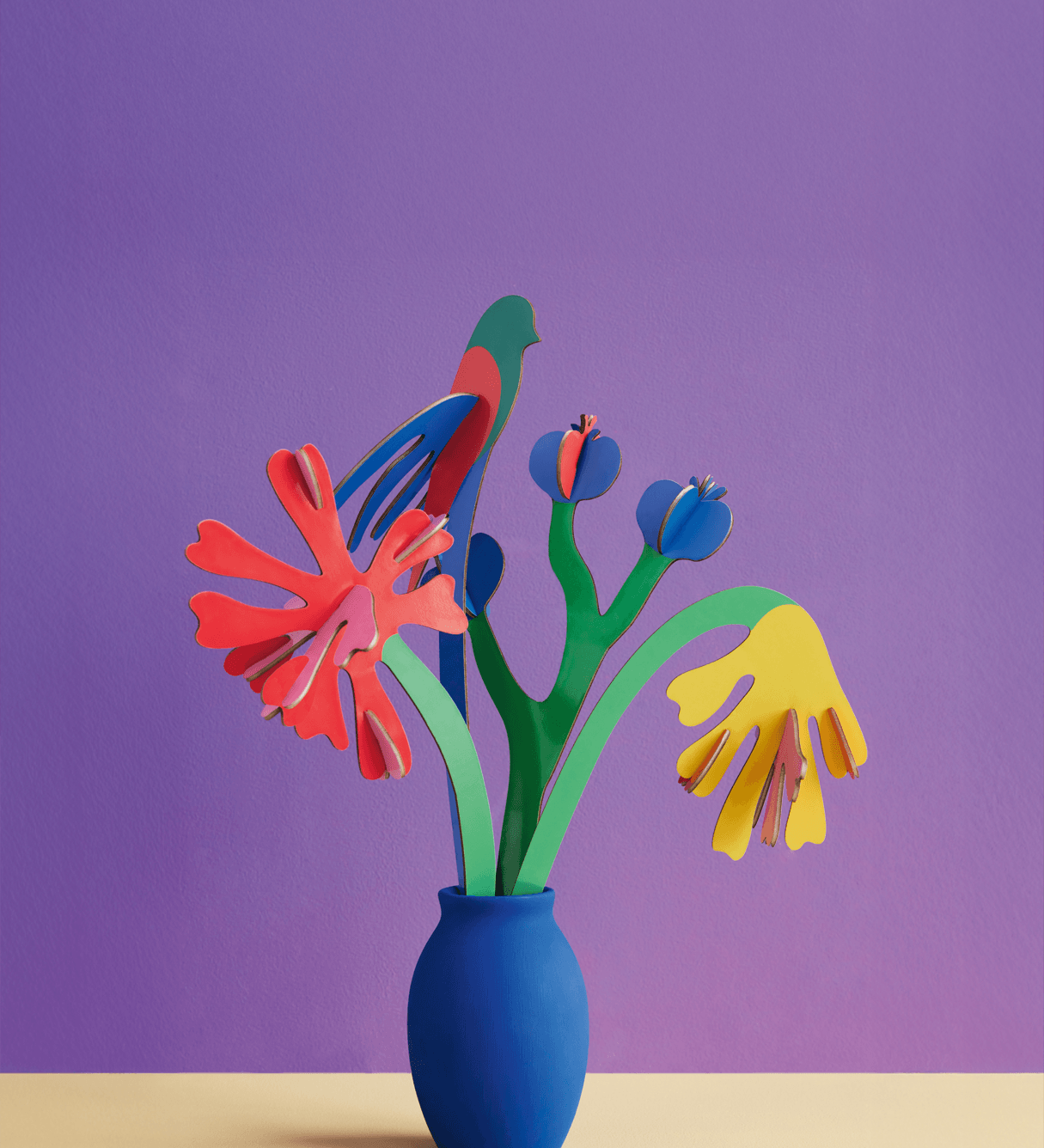 Colorful cardboard flowers in a blue vase against a purple background