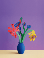 Colorful cardboard flowers in a blue vase against a purple background
