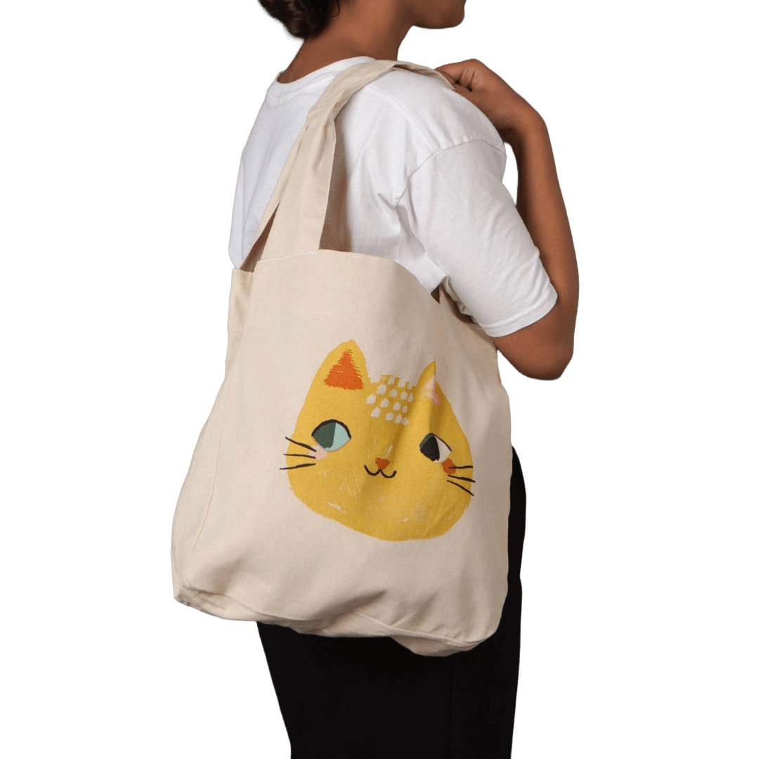 Person carrying a beige tote bag with a cat design 