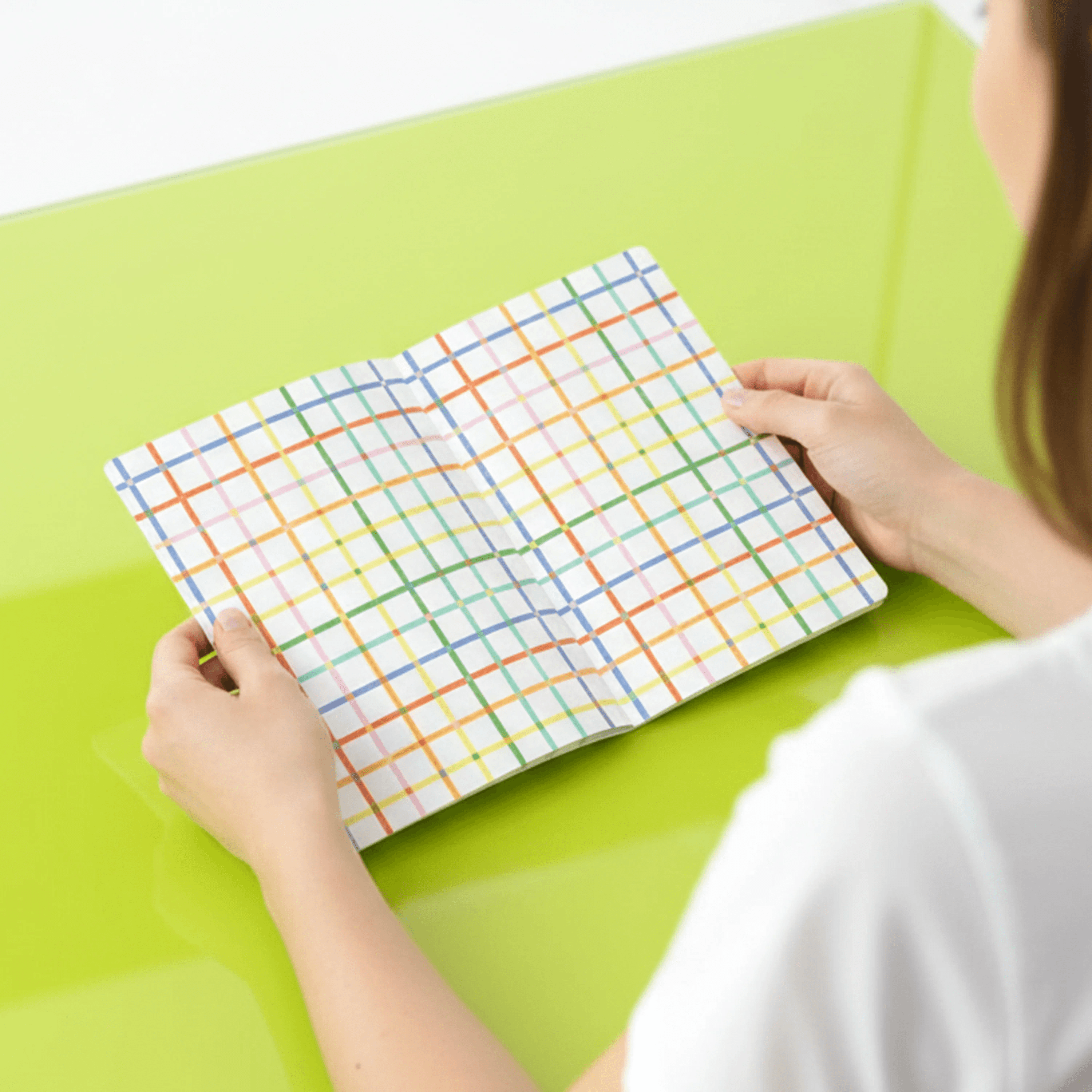 Person holding a colorful grid-patterned notebook on a green surface