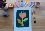 Artistic depiction of a flower with paint tubes, brushes, and a candle on a wooden surface.