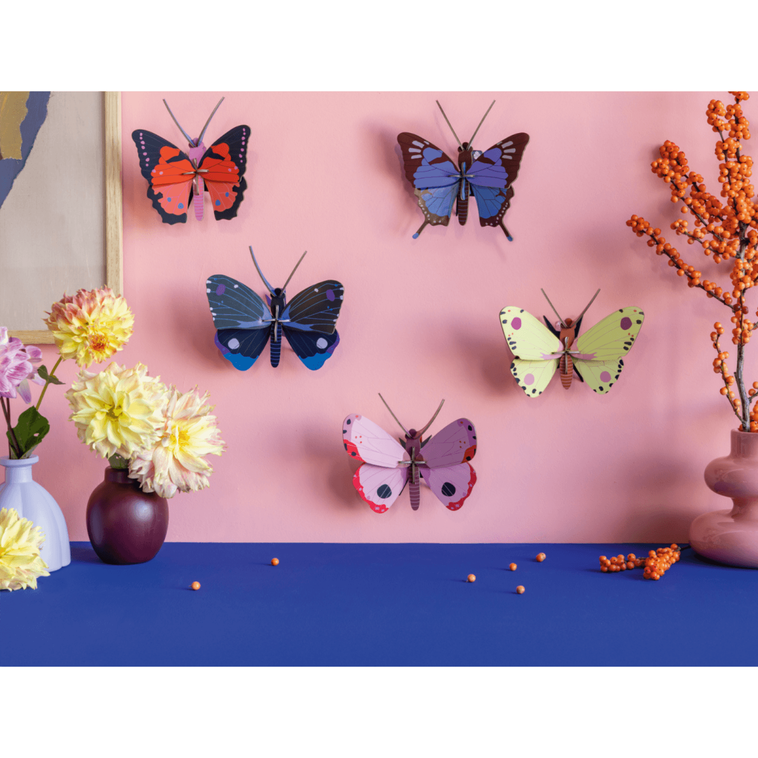 Colorful butterfly decorations on a pink wall with flowers and decorative elements on a blue surface.