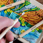Colorful swirled clay with a hand holding small tools on a wooden board.