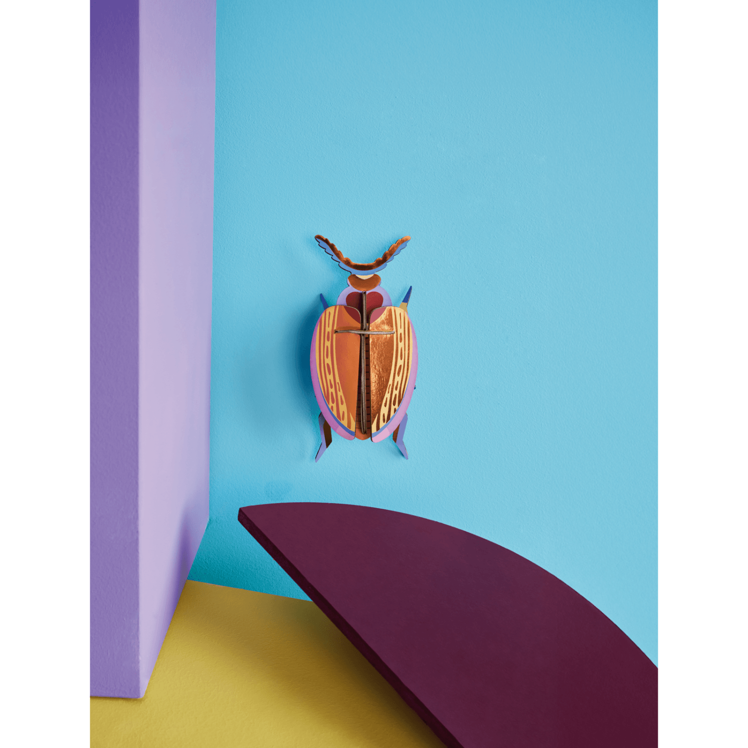 Colorful beetle paper figurine on a blue wall with purple and yellow elements