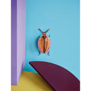 Colorful beetle paper figurine on a blue wall with purple and yellow elements