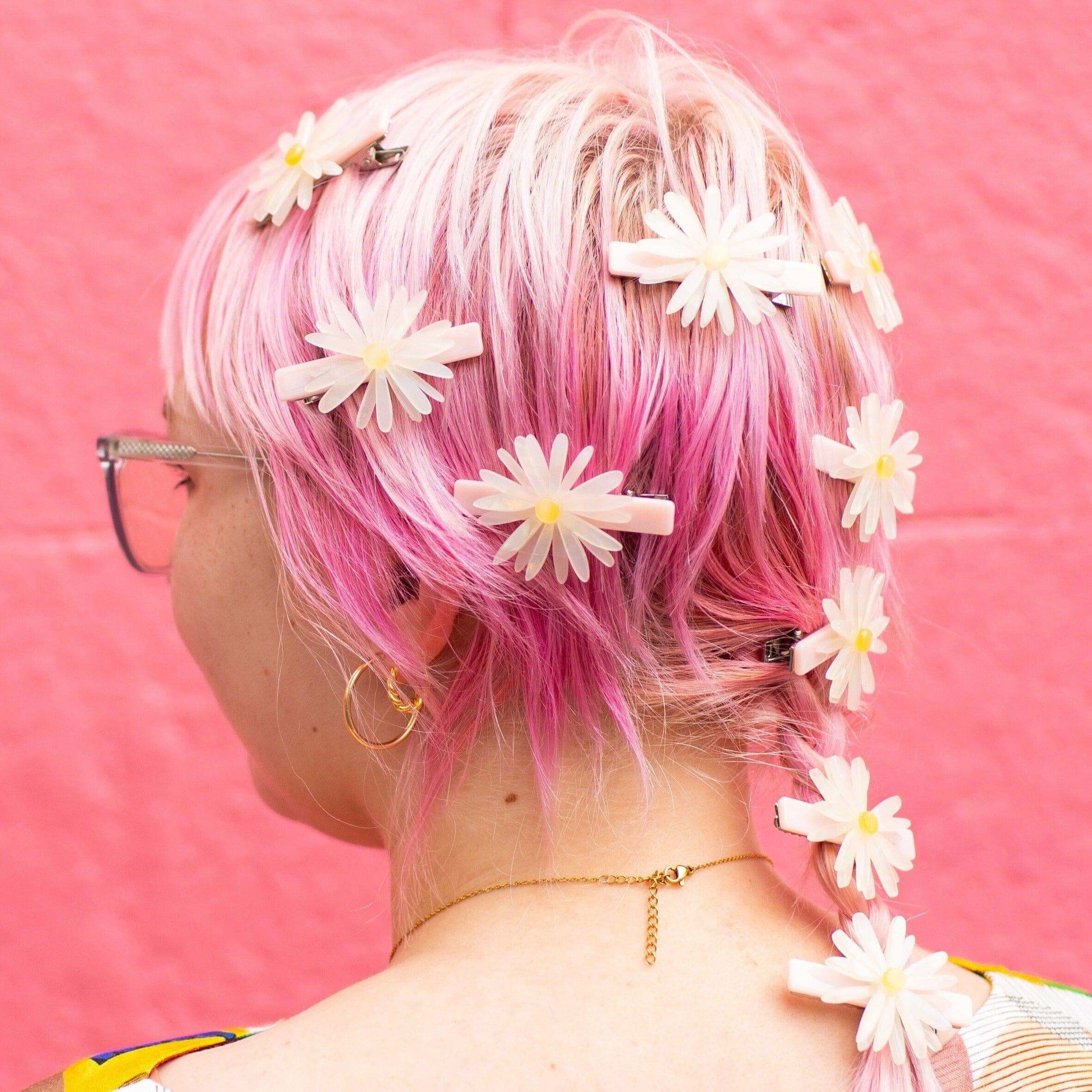 Person with pink hair adorned with white flowers against a pink background