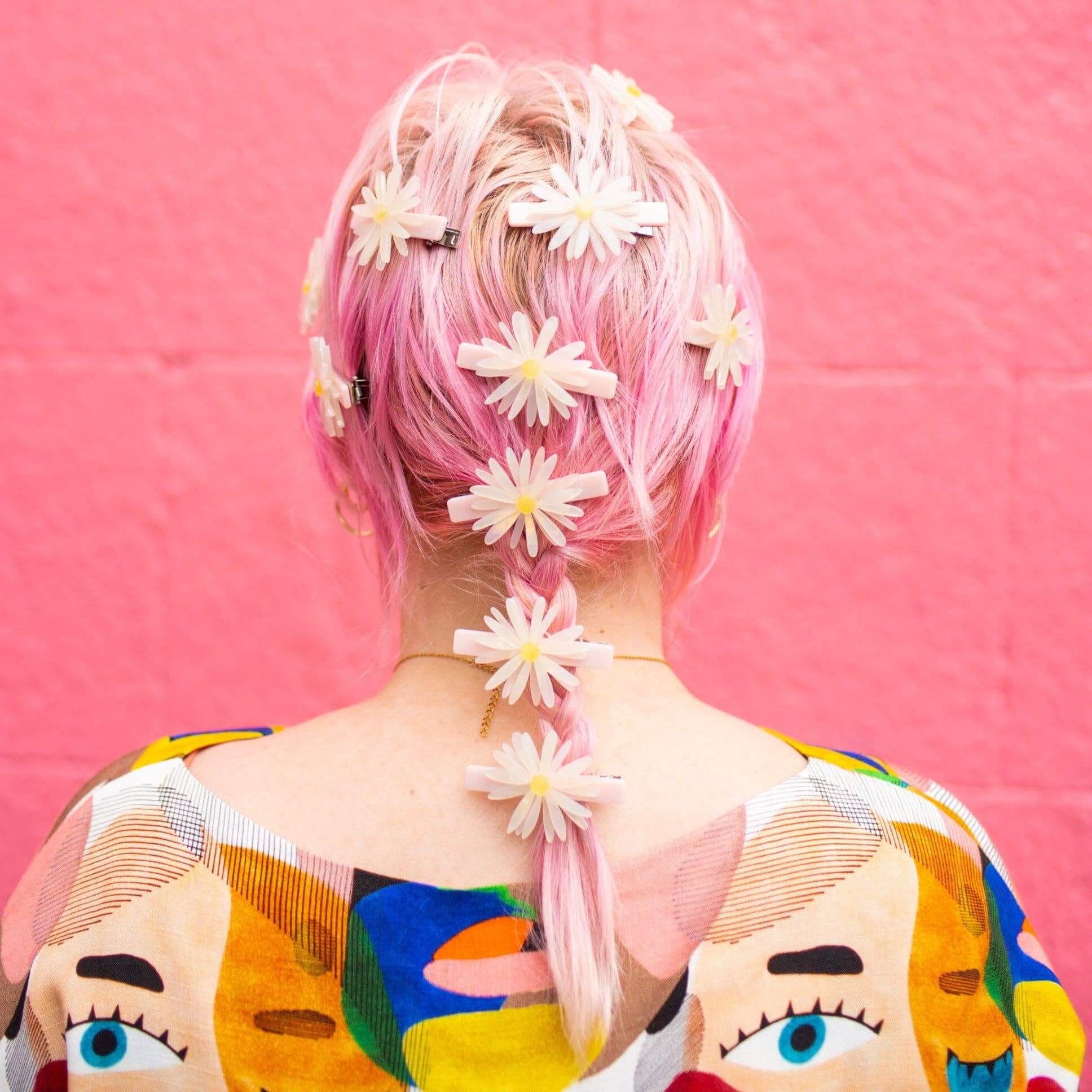 Person with pink hair and floral hair accessories against a pink background
