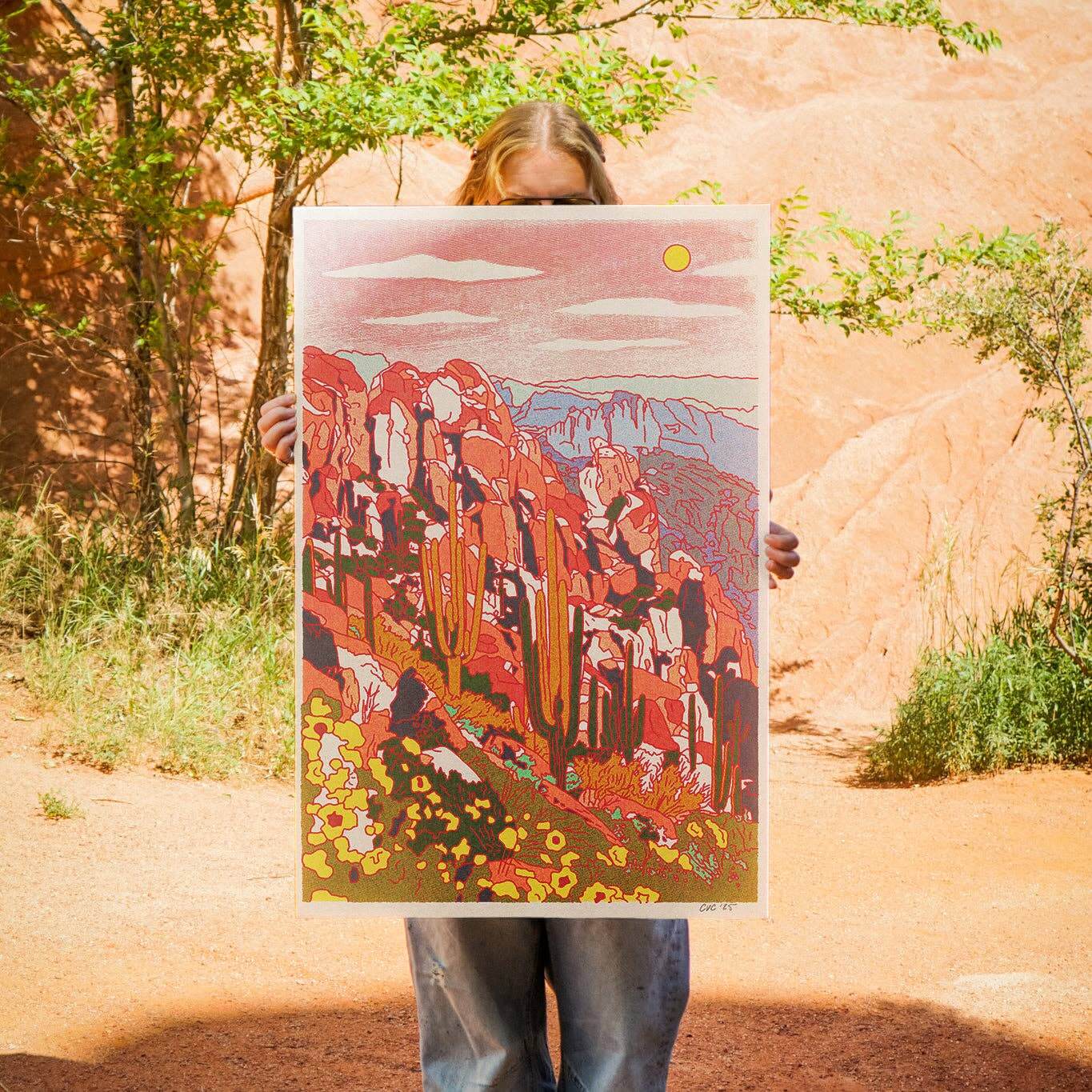 Person holding a colorful landscape print against a natural rock formation background