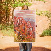 Person holding a colorful landscape print against a natural rock formation background
