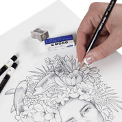 Hand drawing a detailed illustration of a face with flowers and fish using a pencil on a white sheet of paper.