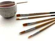 Set of paintbrushes with a ceramic cup on a white surface