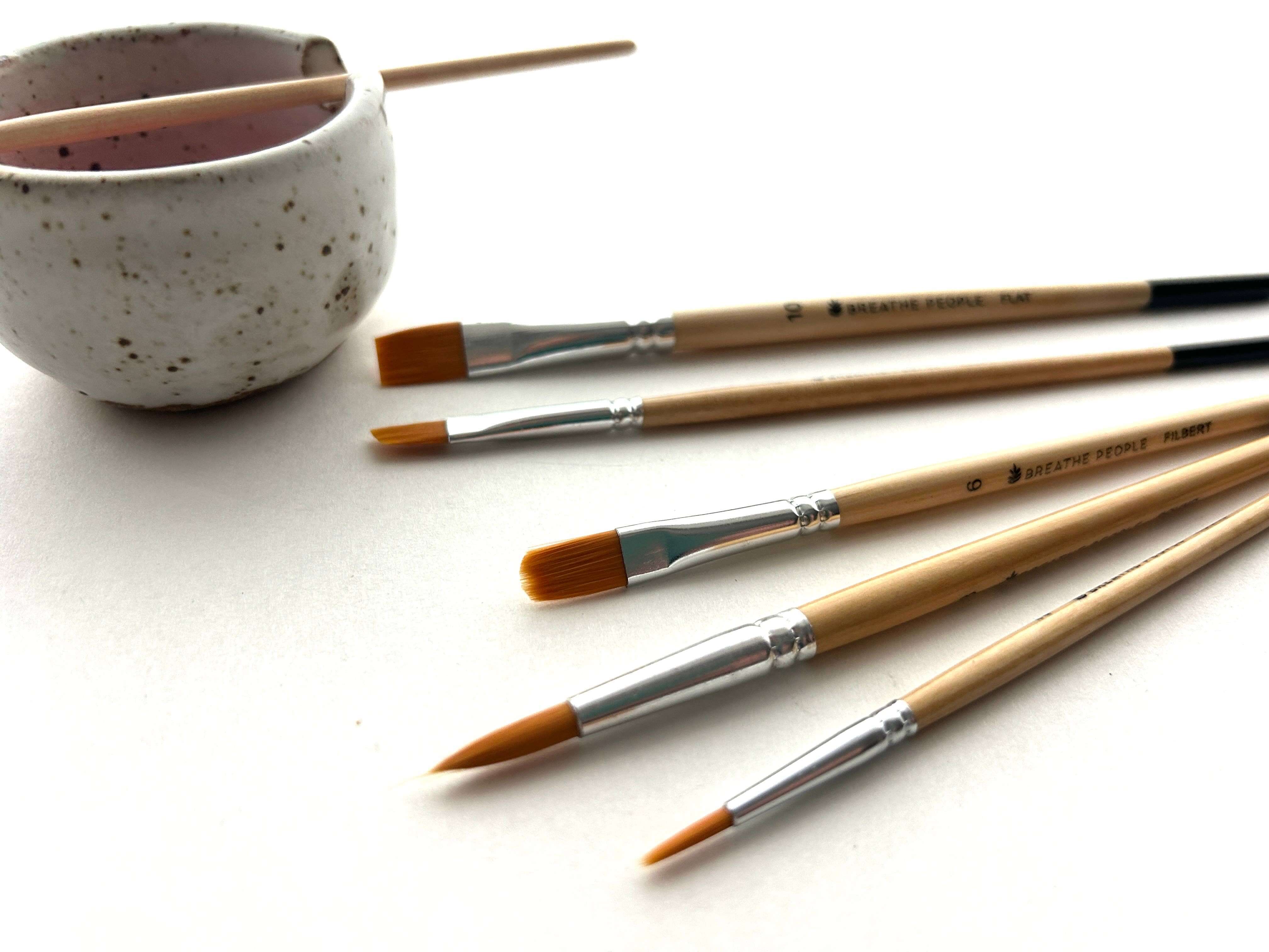 Set of paintbrushes with a ceramic cup on a white surface