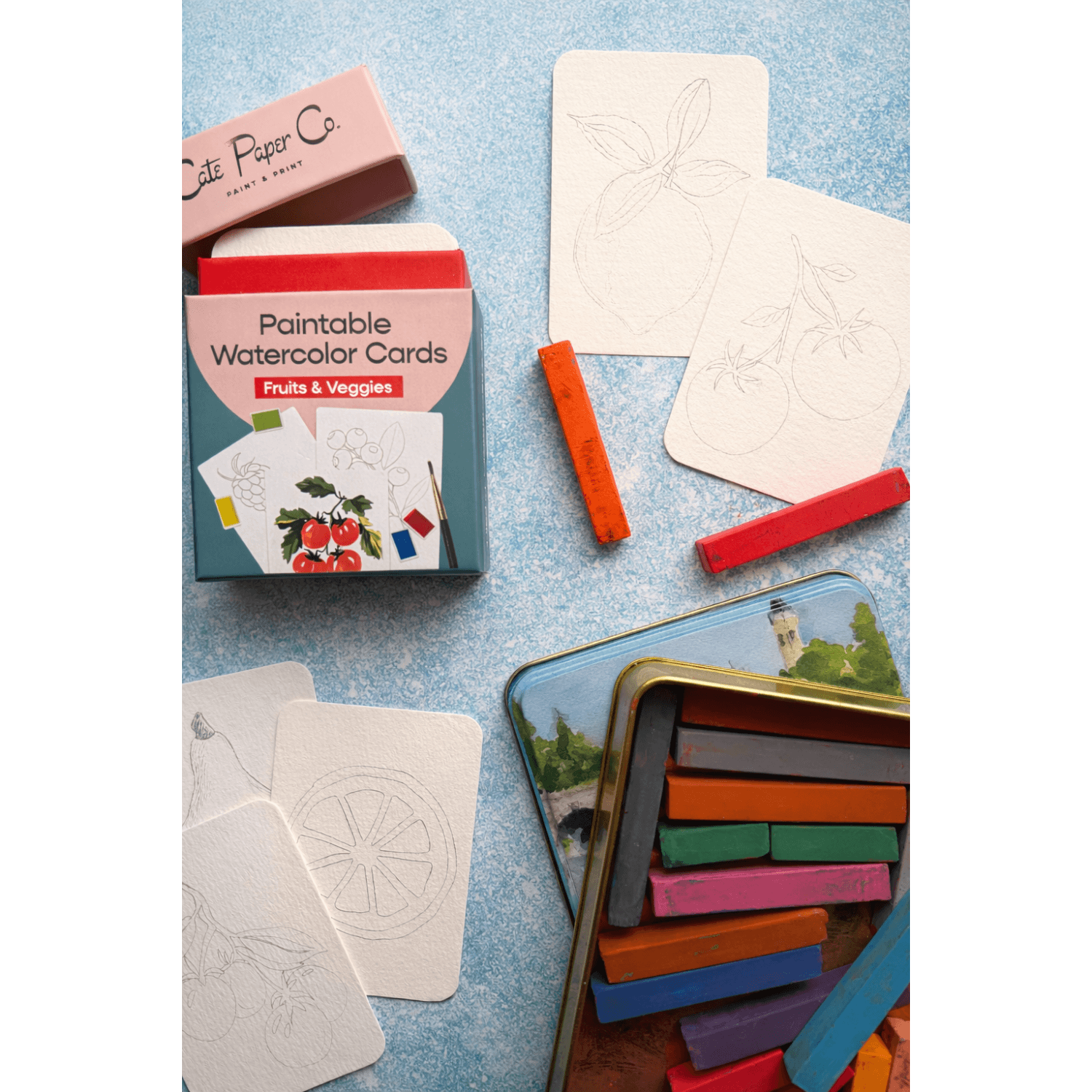 Paintable fruit and vegetable watercolor cards with coloring tools on a blue textured surface