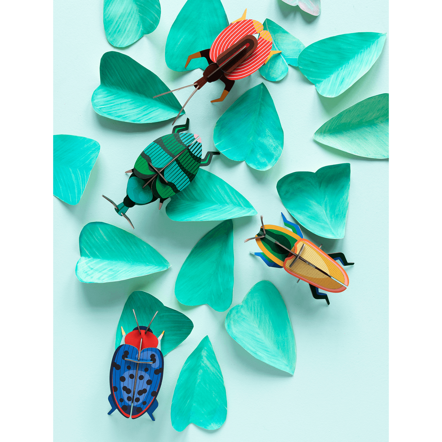 Colorful paper beetles on turquoise leaves against a light blue background