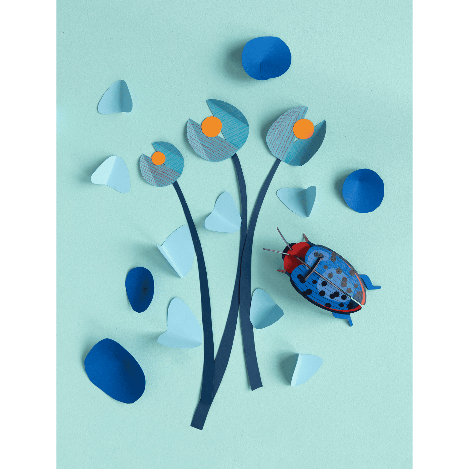Artistic arrangement of paper flowers and a beetle on a light blue background