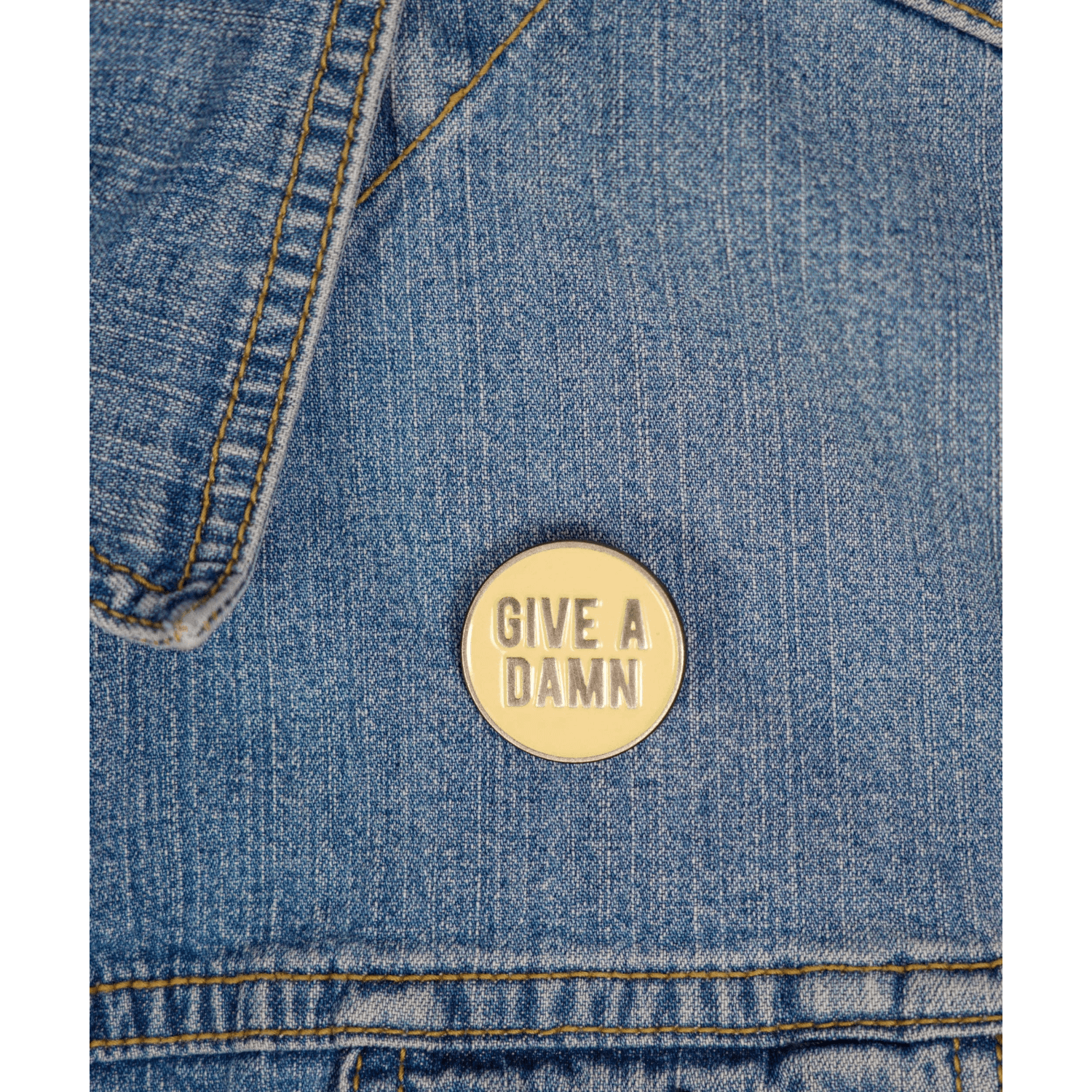 Denim jacket with a beige 'Give a Damn' pin.