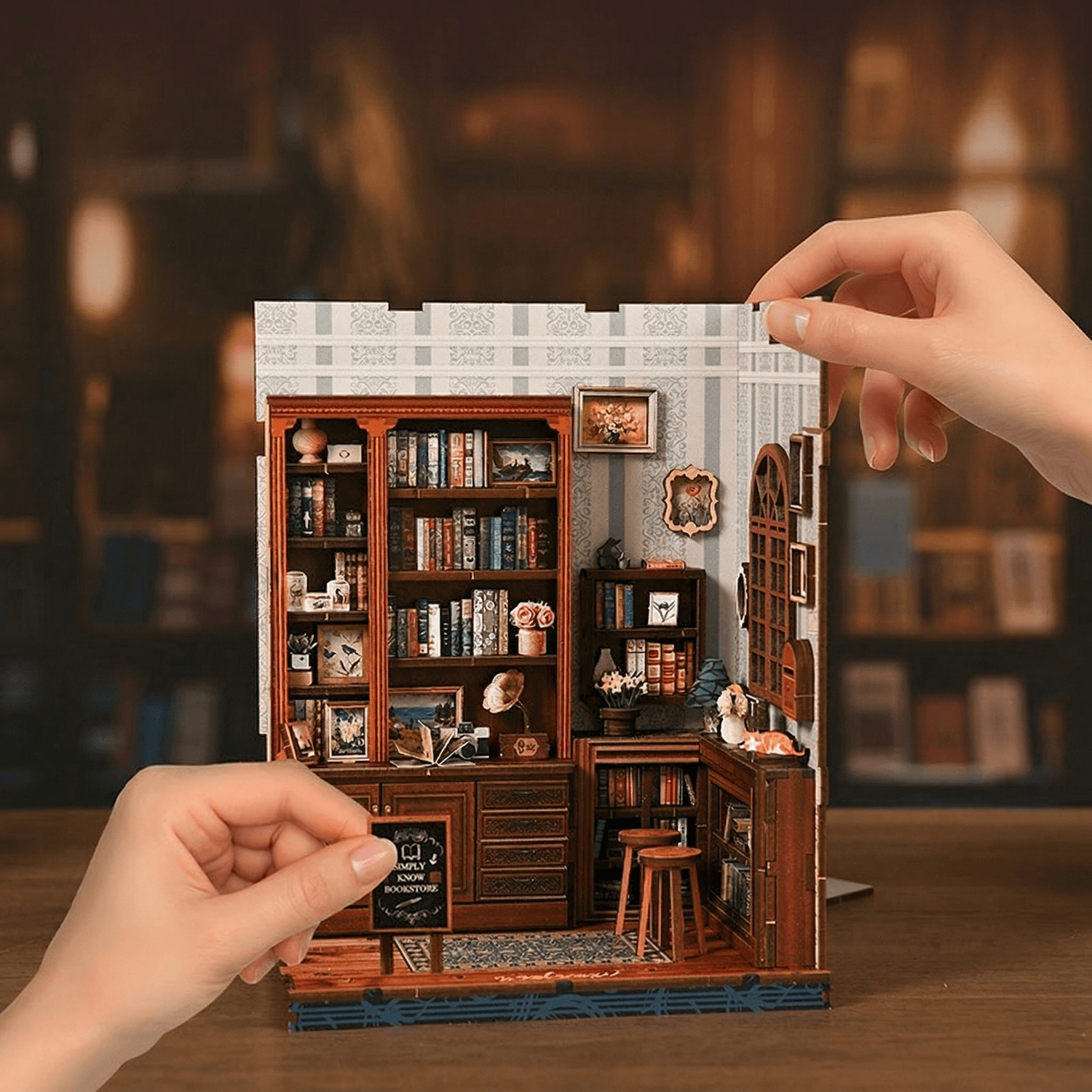 Miniature model of a bookshelf with books and decor, held by hands against a blurred background.