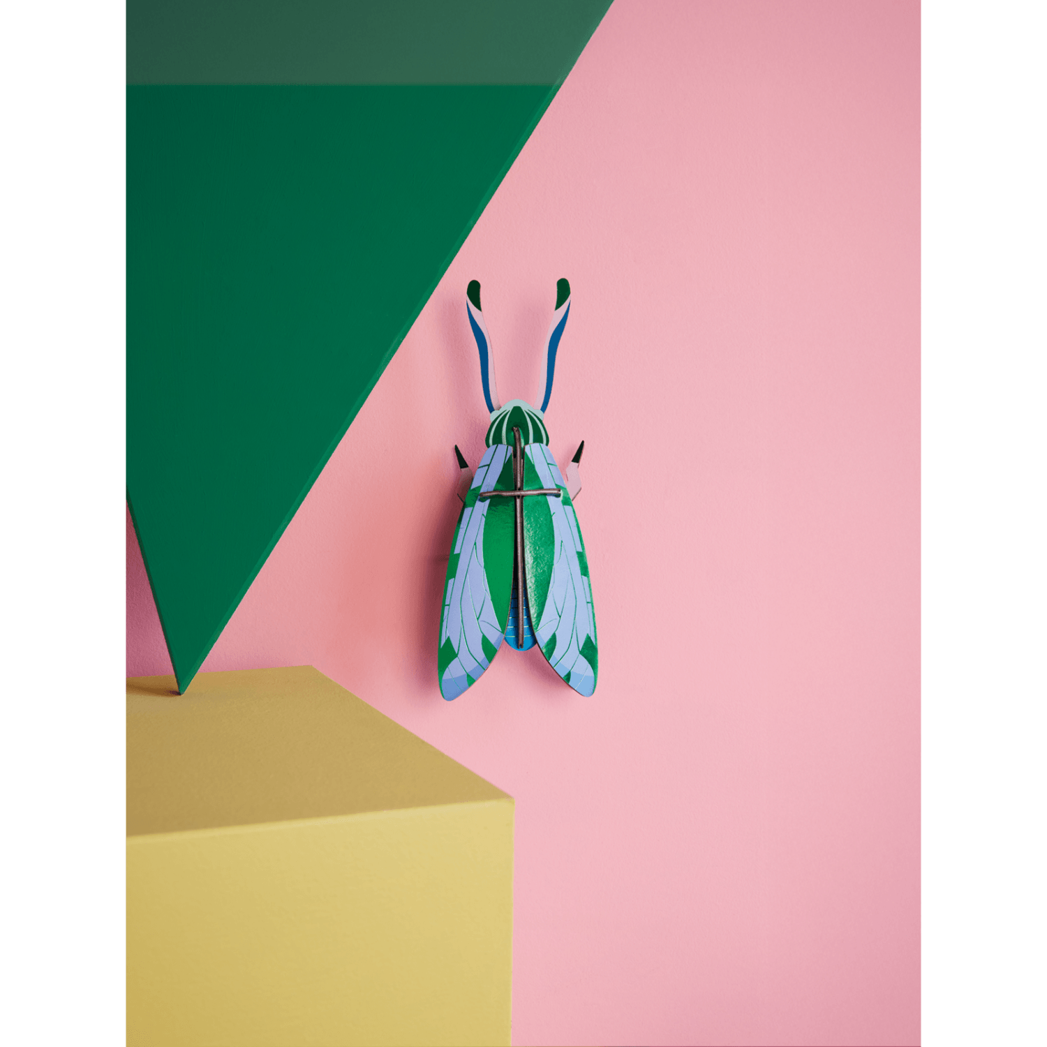 Colorful grasshopper-shaped paper figurine on a geometric pink and green background