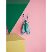 Colorful grasshopper-shaped paper figurine on a geometric pink and green background