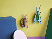 Colorful beetle and grasshopper-shaped wall decorations on a yellow background