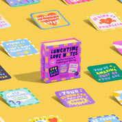 Box of 'Lunchtime Love Notes' on a yellow background with colorful cards around it.
