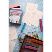 Paintable watercolor cards with a tin of paint sticks on a textured blue surface.