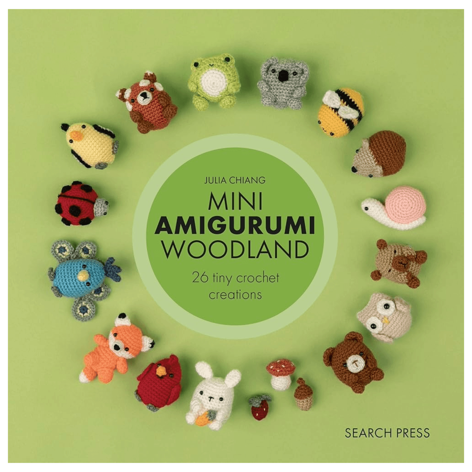 Book cover for 'Mini Amigurumi Woodland' by Julia Chiang, featuring a circle of small crocheted woodland animals arranged around a green center title circle on a light green background. Visible text includes '26 tiny crochet creations' and 'SEARCH PRESS'.