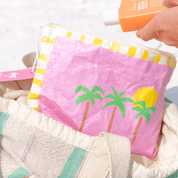 Pink pouch with palm tree design with a beach set up.