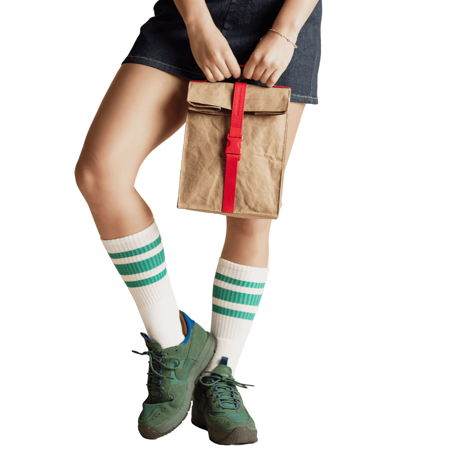 Person holding a brown paper bag with a red strap, wearing green sneakers and white socks with green stripes.