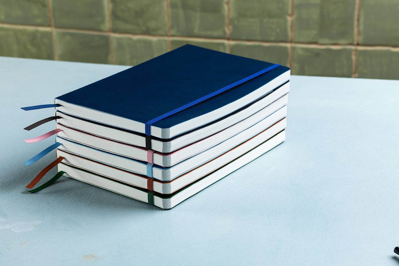 Stack of notebooks with colorful ribbons on a light blue surface