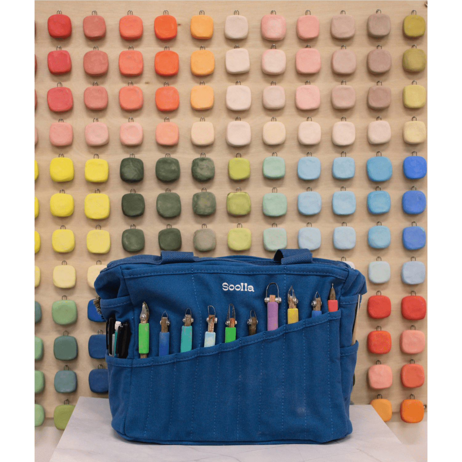 Blue painter's bag with colorful tools against a colorful pegboard background