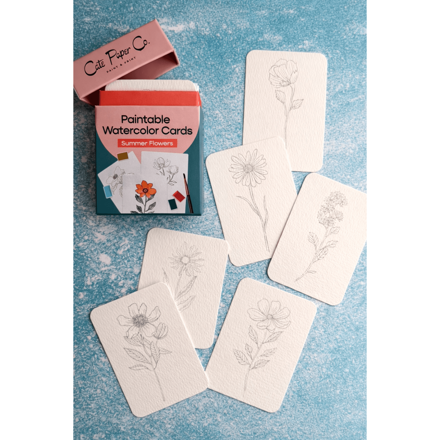 Set of flower paintable watercolor cards with a Cate Paper Co. packaging on a blue textured background.