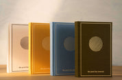 Four 'the good day journal' books in different colors on a wooden surface with a light background.