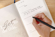 Hand writing in a journal with a pen on a wooden surface