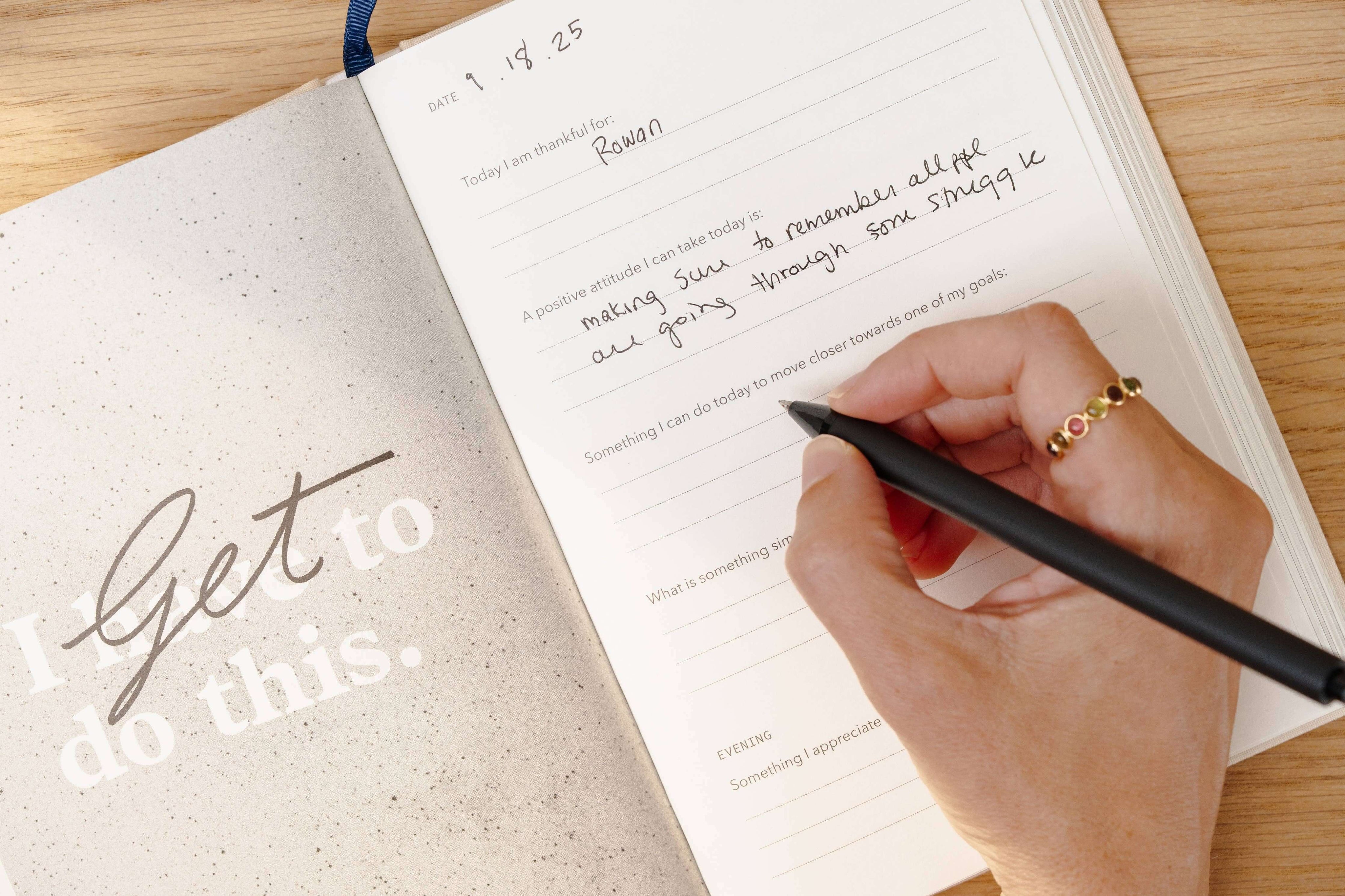 Hand writing in a journal with a pen on a wooden surface