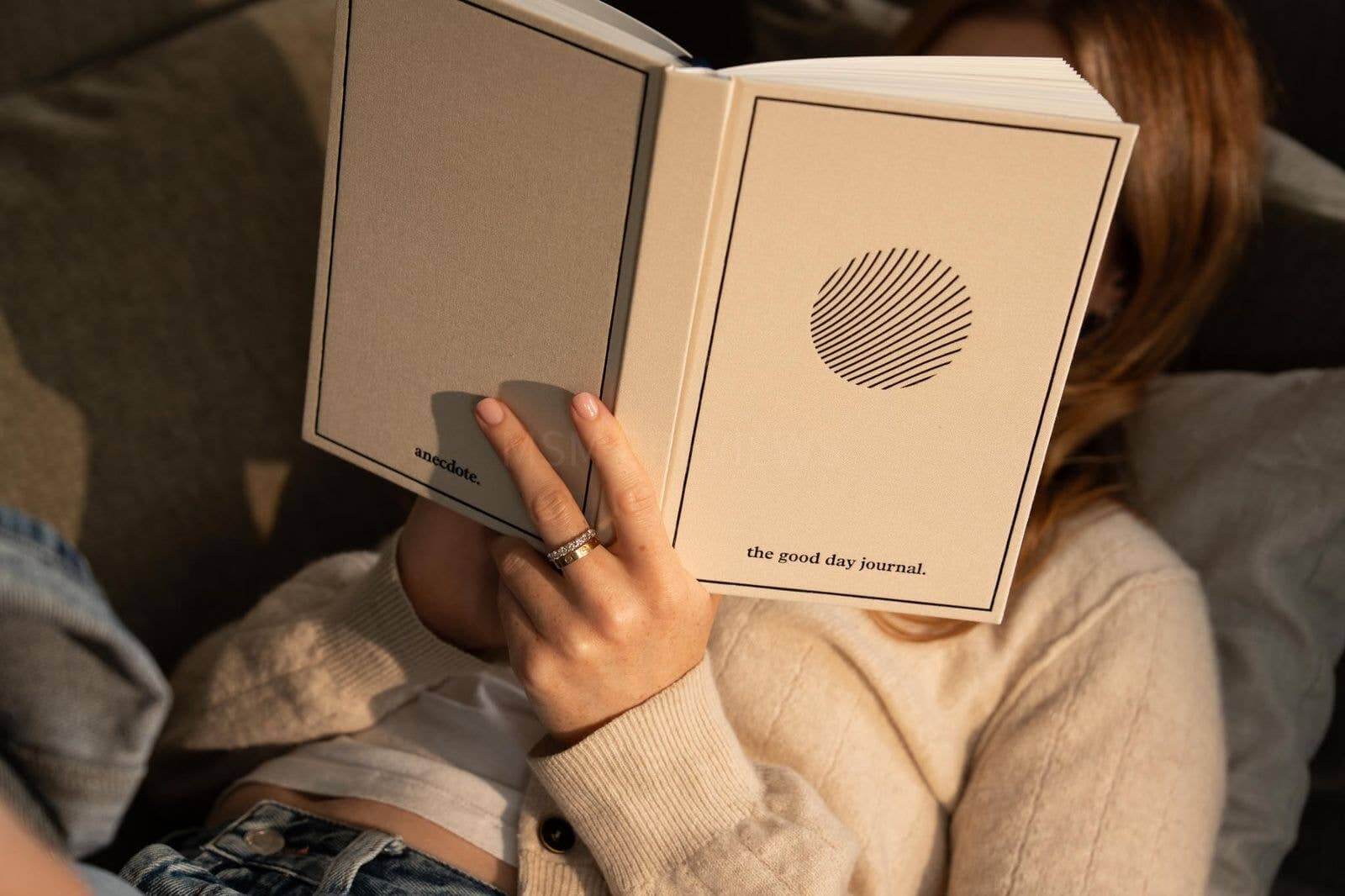 Person holding 'The Good Day Journal' book with a circular design on the cover.