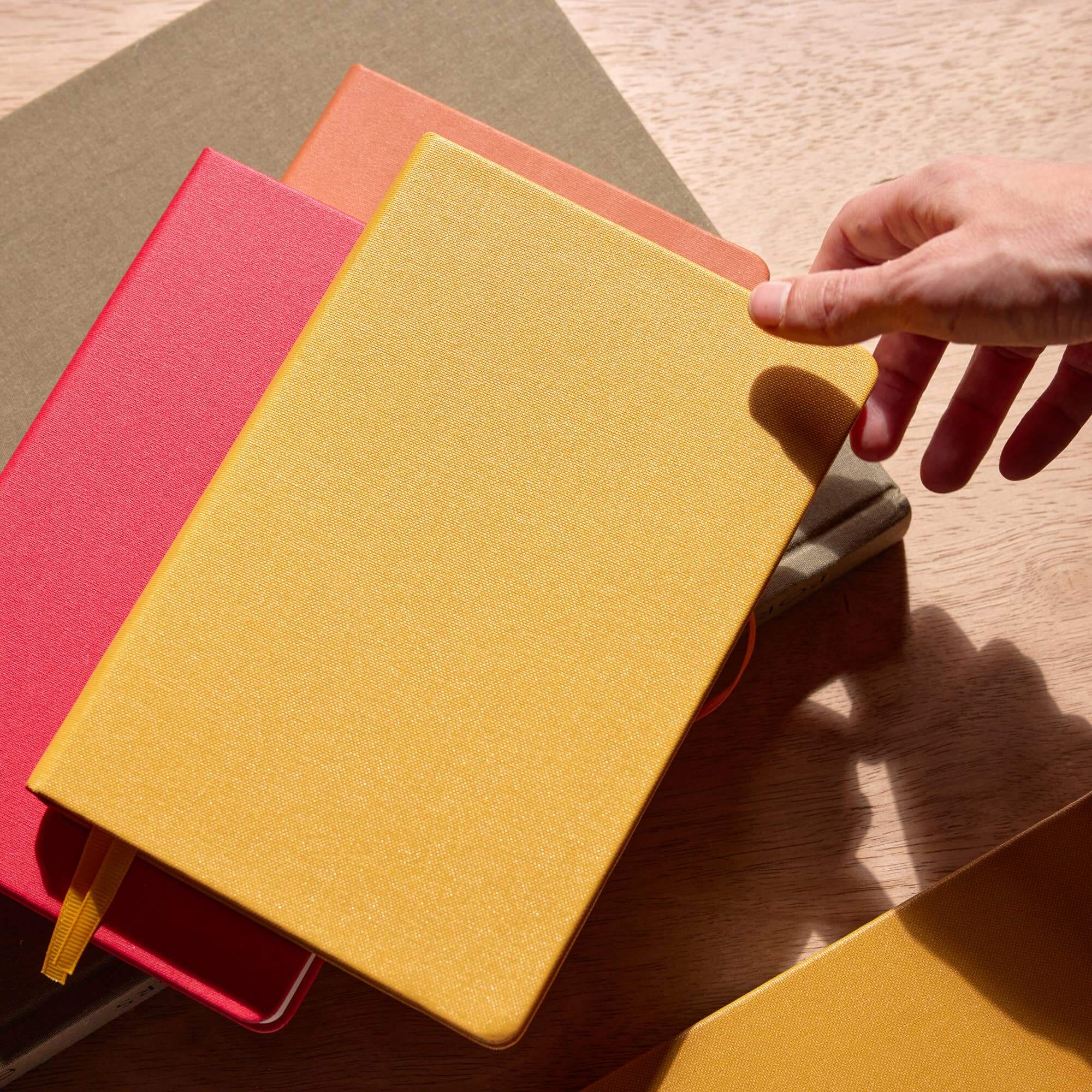 Hand interacting with a yellow notebook among other colorful notebooks on a wooden surface