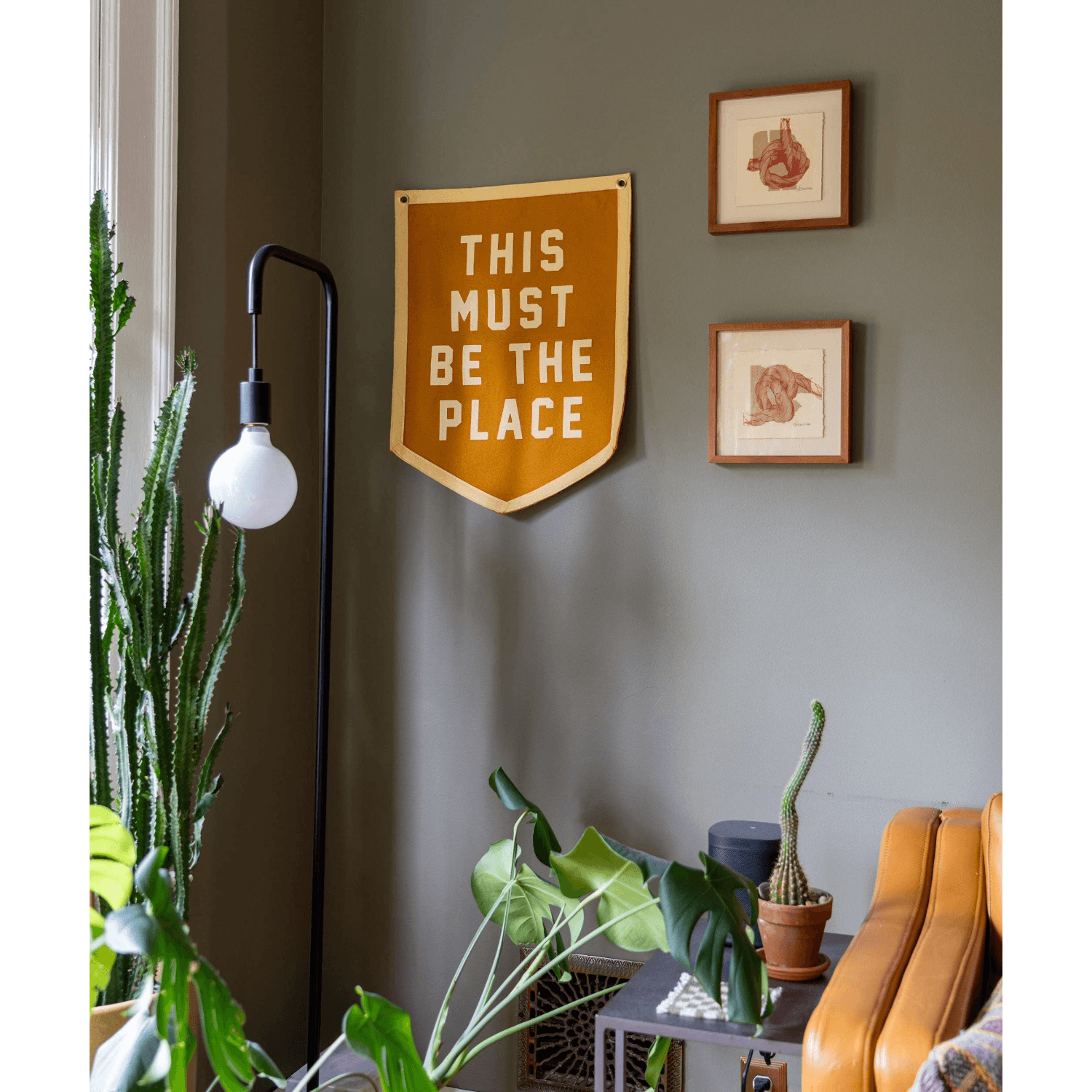 Decorative sign on a wall with plants and a lamp in a room.