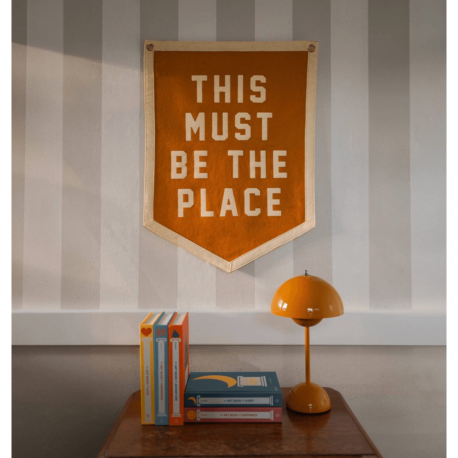 Decorative banner with 'THIS MUST BE THE PLACE' text on a wall above books and a lamp.