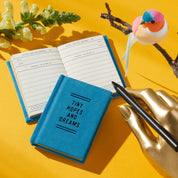 Blue notebook with 'Tiny Hopes and Dreams' text on a yellow background with a pen and decorative elements.