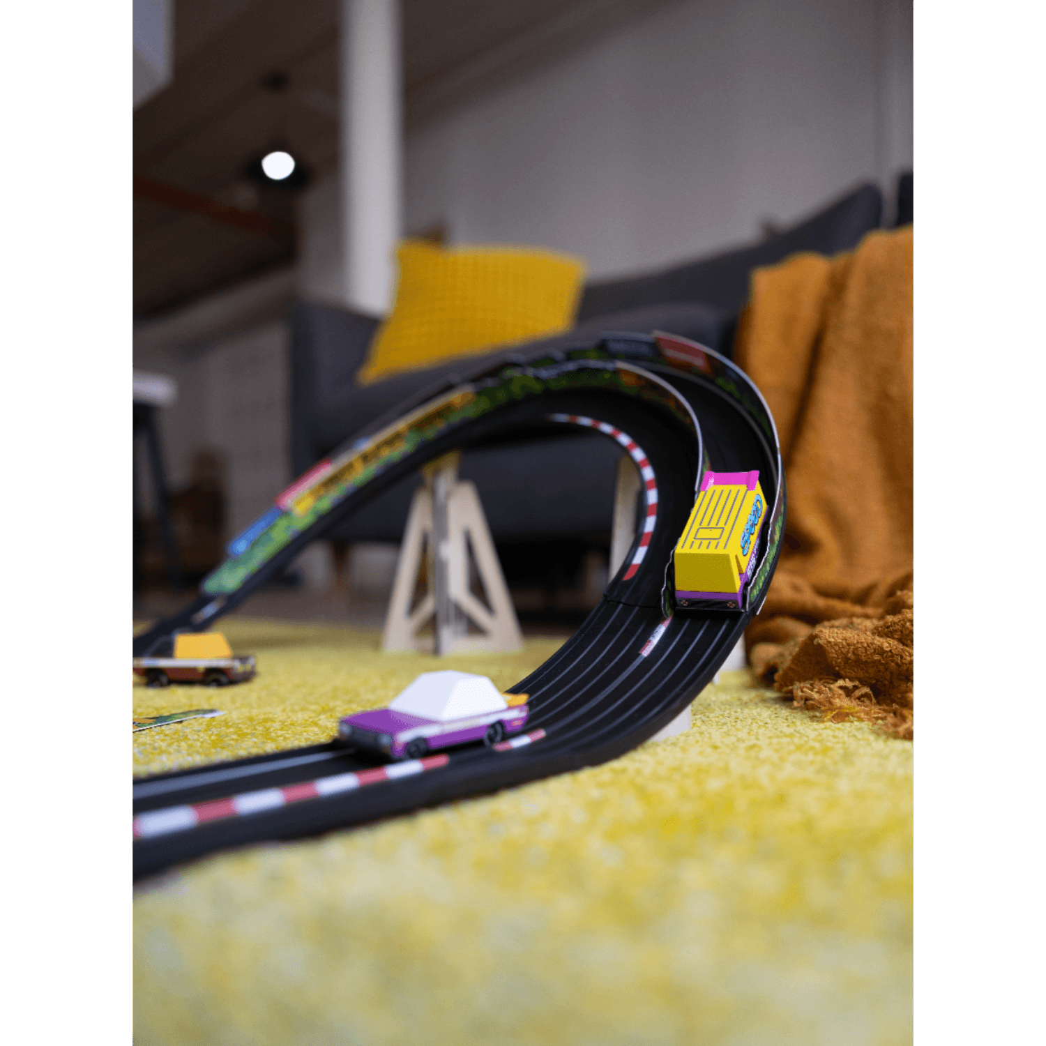 Toy car track set on a yellow carpet with toy cars on a blurred indoor background