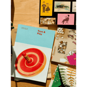 Book titled 'Toys & Play' with a red and yellow toy on a blue cover, displayed on a wooden surface with other items.